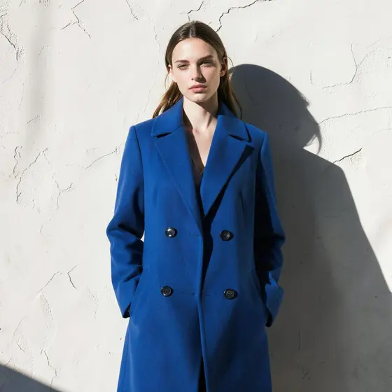 Model in a cobalt blue coat against a sunlit plaster wall